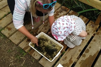 Adult and child looking in a tray of water and weed to see what came out of the pond.