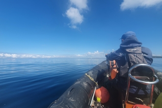 Our warden, Leighton, in the front seat of a RIB planing over flat waters.