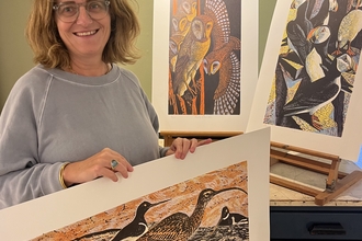 Emma Mason holding curlew print with more artwork on display in the background. 