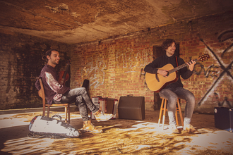 Filkin's Drift sit in a concrete room playing their instruments. The atmosphere is relaxed and sunlight streams in.
