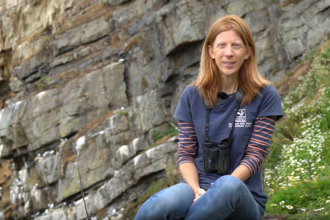 Lisa sat on a cliff with a seabird colony behind her. 