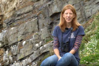 Lisa sat on a cliff with a seabird colony behind her.