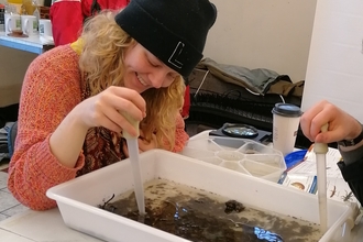 A woman is smiling while sat at a desk working on a river invertebrate sample 