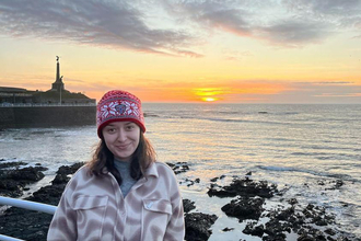 A woman stood by the coast at sunset. 