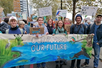 A group of young people in a crowd at the March for Water event. They are holding a big banner which says 'our rivers, our future' and placards that read 'Save Our Taff'..