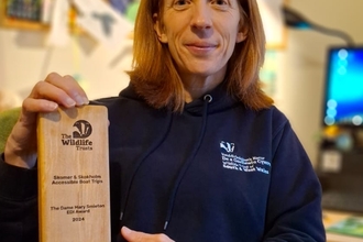 Lisa Morgan, Head of Islands and Marine Conservation, holding the Dame Mary Smeiton Award which reads 'Skomer and Skokholm Accessible Boat Trips' and features the Wildlife Trust logo. 