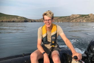 Rob driving a boat with Skomer Island in the background. 