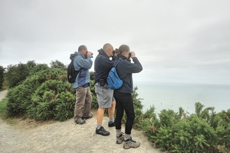 Attendees looking through binoculars from a coastal cliff