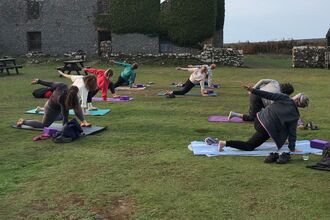 A group of people doing stretches on yoga mats in the courtyard. The ruined farmhouse is behind them.