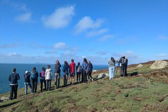A group of people on a path looking away from the camera out to sea.