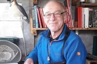 Steve Sutcliffe reading a book with binoculars around his neck