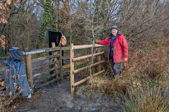 John Wilson in a red rain jacket with a reparied kissing gate at Ystradfawr