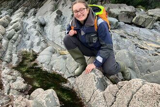 A woman crouched over a rockpool. She is smiling at the camera.