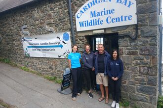 A group of people standing in front of Cardigan Bay Marine Wildlife Centre, a stone building with a CBMWC sign.