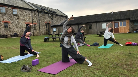 Four people do a yoga position in the courtyard on Skomer