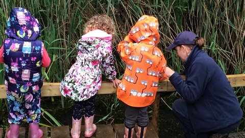 3 small children and one adult looking into a small pond