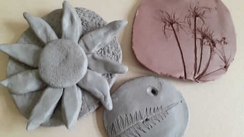 3 clay tiles showing leaves and a flower head