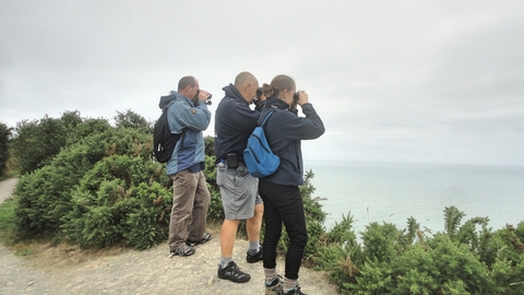 Attendees looking through binoculars from a coastal cliff
