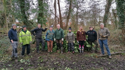 A group of staff and volunteers stood next to a pile of cleared vegetation in Roath Wild Gardens