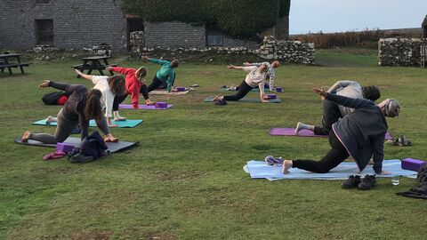 A group of people doing stretches on yoga mats in the courtyard. The ruined farmhouse is behind them.