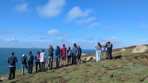 A group of people on a path looking away from the camera out to sea.
