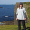 Lizzie standing in front of a coastal cliff - the sea is deep blue. 