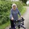 A woman stood with a walking aid on a path with rich green verges on each side. 