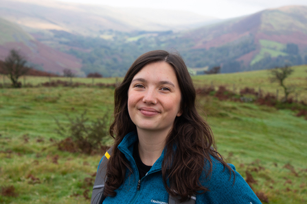 Alice, our Assistant Conservation Officer, standing in field with mountains behind her. 