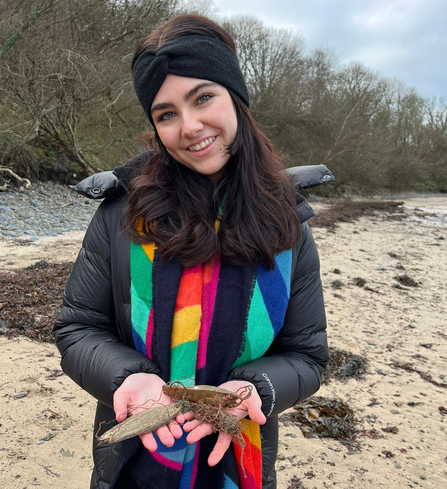 Grace holding some shark egg cases in her hand at a beach. 