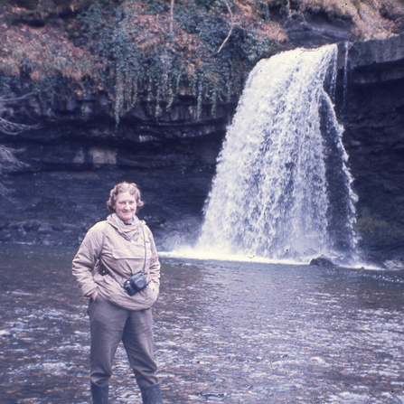 Dr Mary Gillham standing in front of a waterfall. 