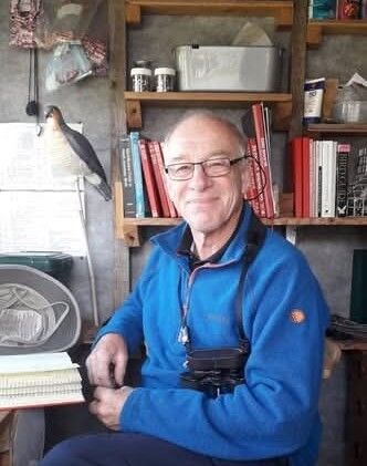 Steve Sutcliffe reading a book with binoculars around his neck