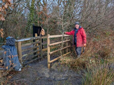 John Wilson in a red rain jacket with a reparied kissing gate at Ystradfawr
