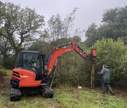 A digger with a hydraulic fence post driver attachment putting in a fence