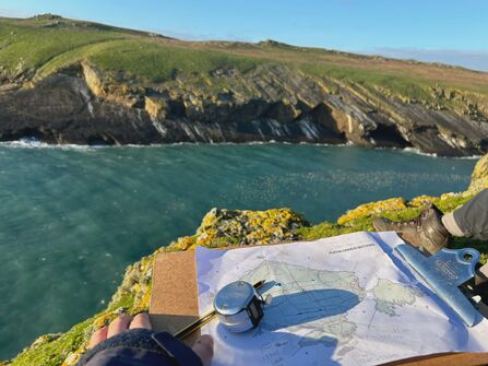 A clipboard with a map of Skomer and a clicker, with the sea and cliffs in the background. 