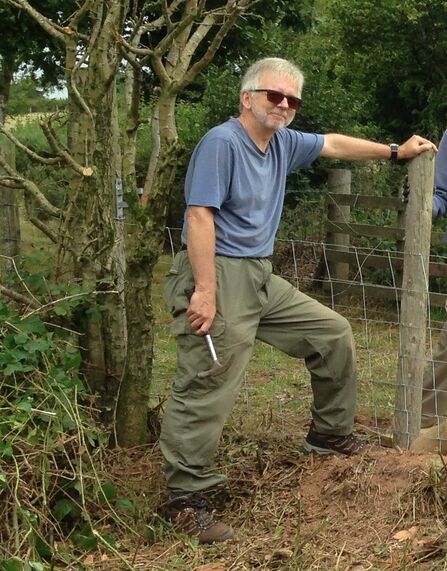 A man leaning on a fence. There are trees in the background.