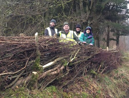 4 people in high vis clothing stood behind a hedge