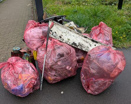 A large pile of full bags of rubbish and a litter picker.