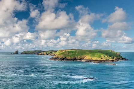 A green island surrounded by blue seas and cloudy skies. 