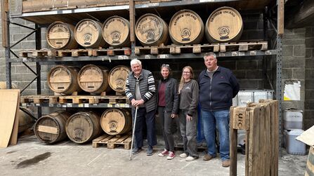 lots of sasks of whiskey with a group of people standing in front, including Johnny and Andrea. 
