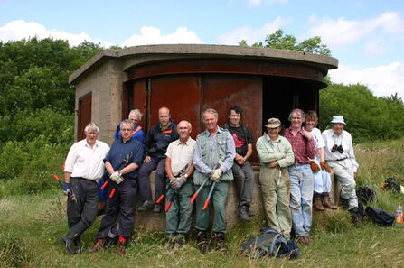 A group of people stood together in a nature reserve holding gardening tools.