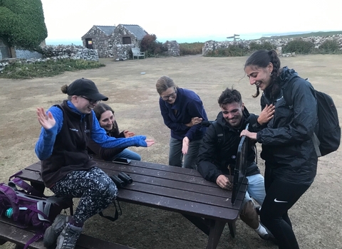 5 weekly volunteers sat in the courtyard on a picnic bench, laughing and looking at moths.