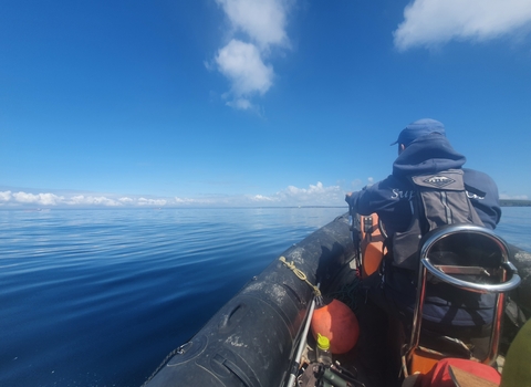 Our warden, Leighton, in the front seat of a RIB planing over flat waters.