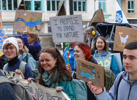 Young people in a crowd at the March for Water event. They read signs that say 'I promise to stand for nature'. 