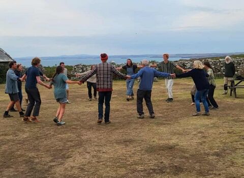 A group of people holding hands in the courtyard for the island ceilidh. There are musicians playing to the side.